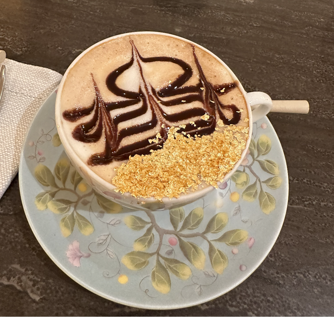 Cappuccino with decorative foam art on a floral saucer with edible gold leaf